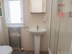 Ein Badezimmer mit Toilette, Waschbecken, Handtuchhalter, einem Fenster mit Jalousien und einem Spiegel.