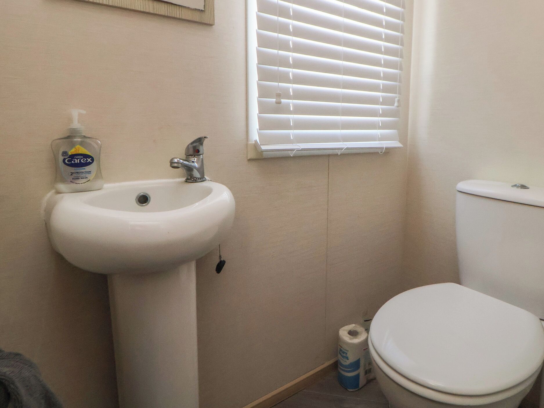 A bathroom with a white sink, a toilet, and a window with blinds.