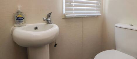 A bathroom with a white sink, a toilet, and a window with blinds.