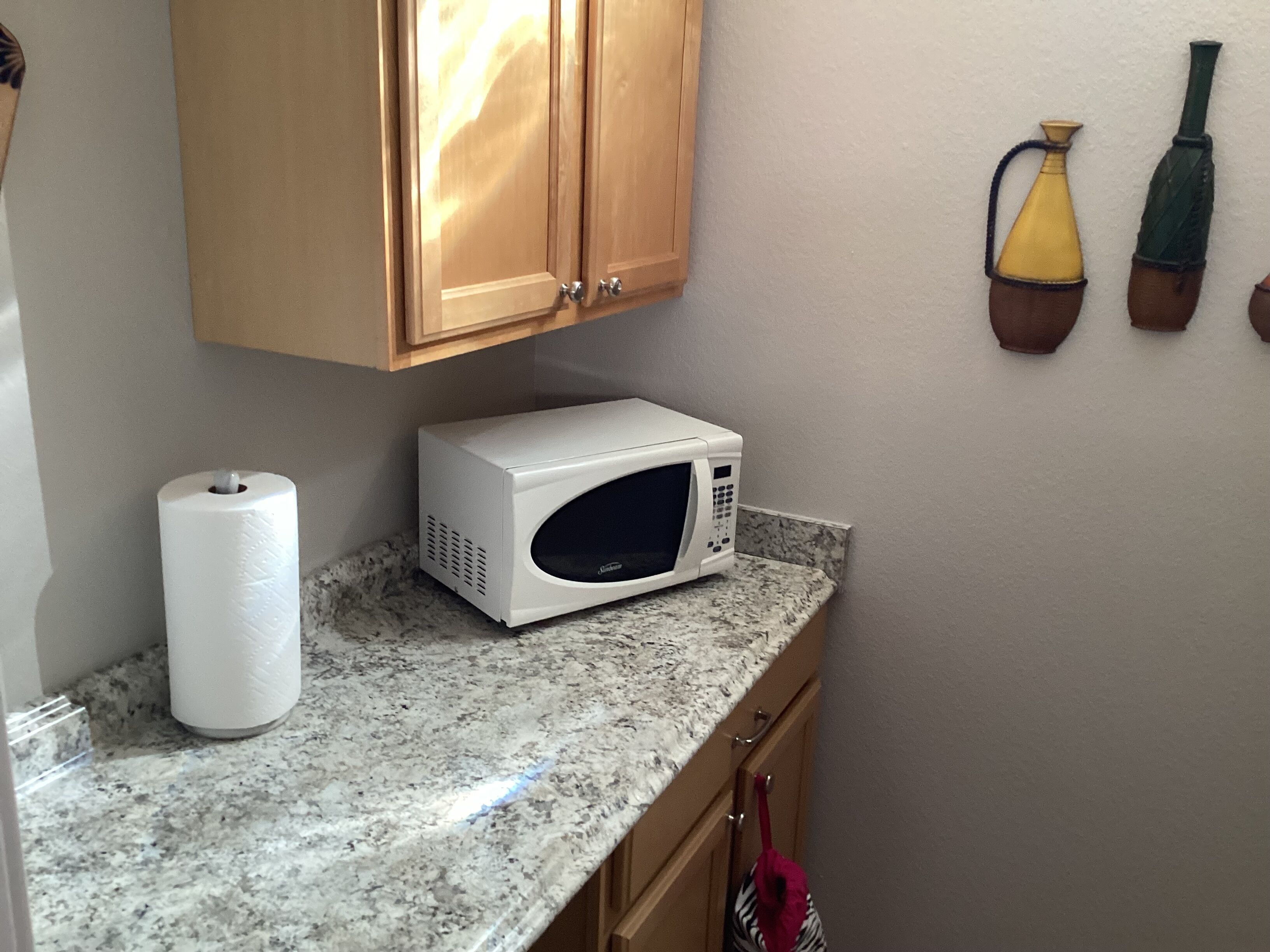 A kitchen with wooden cabinets, a white microwave on a granite countertop, and a roll of paper towels.