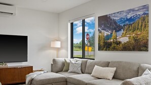 Una sala de estar con un sofá modular, un televisor de pantalla plana, una lámpara y un ventanal con vistas a montañas y un lago.