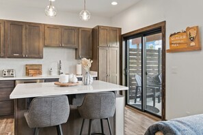 A modern kitchen with wooden cabinets, a marble island, and a view of Glacier National Park. - Peaks & Pines - Sweeping Mountain Views (Columbia Falls)