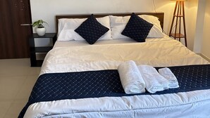 A neatly made bed with white and navy bedding, a decorative fan, and a bedside lamp.