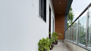 A clean, modern corridor with white walls and a shiny tiled floor. There are several potted plants along the wall, and a glass railing on the right side.