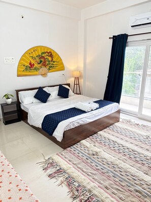 Une chambre à coucher bien aménagée, avec un lit, des tables de chevet, une lampe sur pied, un ventilateur décoratif et une grande fenêtre avec des rideaux.