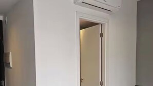 Una habitación de hotel con una cama, un aire acondicionado instalado en la pared y una puerta que da a otra habitación.
