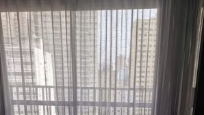 Una habitación con un ventanal cubierto por cortinas translúcidas, una cama y un mueble oscuro.