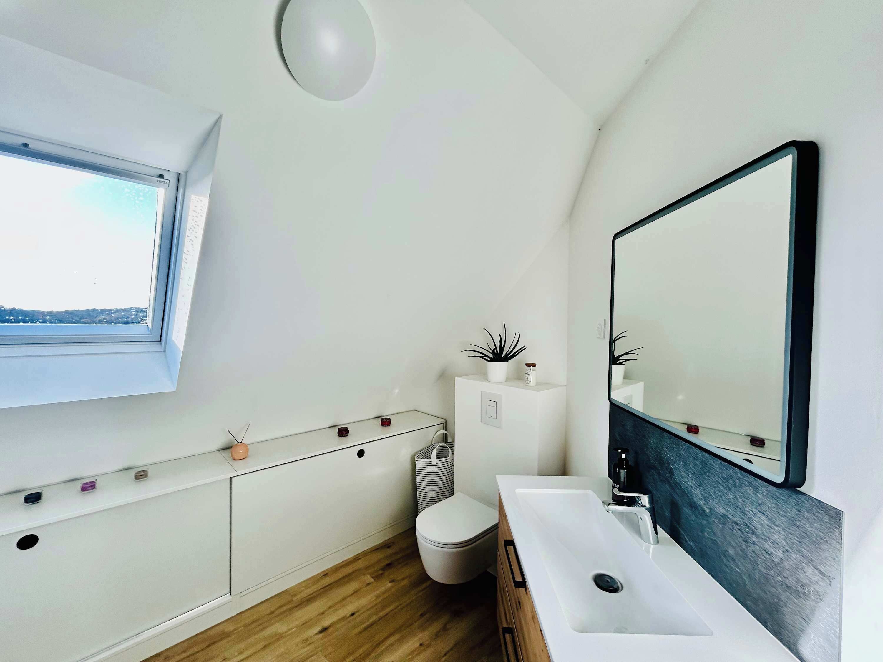 A modern bathroom with a window, a white sink, a mirror, and a toilet.