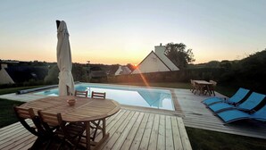 Zona de piscina amb terrassa de fusta, gandules i taula amb seients.