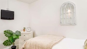 A bedroom with a bed, a window, a television, a dresser, and a potted plant. - Boatman's Cottage Mousehole- Sleeps 4 -Garage (Mousehole)