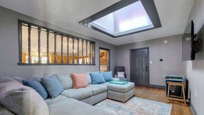 Una sala de estar moderna con un amplio sofá modular, un tragaluz, piso de madera y una pequeña mesita.