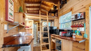 Una cocina compacta con paredes de madera, un microondas integrado y una escalera para almacenamiento en altura.