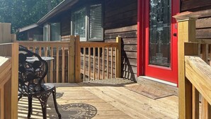 A wooden deck with a red door, a table with chairs, and a window with blinds. - Farm Suite, King bed, overlooking horse pasture! (Asheville)