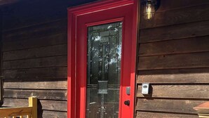 A wooden cabin with a red door, a small porch, and a welcome mat. - Farm Suite, King bed, overlooking horse pasture! (Asheville)