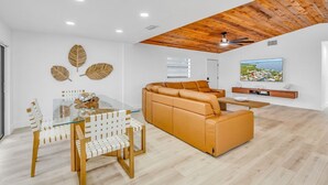 Ein modernes Wohnzimmer mit einem Glastisch, Holzstühlen, einem Ledersofa und einer Holzbalkendecke.