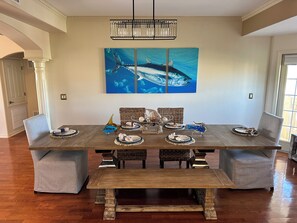 A dining room with a wooden table, grey upholstered chairs, and a large shark-themed painting on the wall.