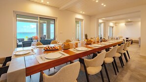 Ein langer Esstisch ist für eine Mahlzeit gedeckt, mit Stühlen, Blick auf einen Balkon und modernem Interieur.