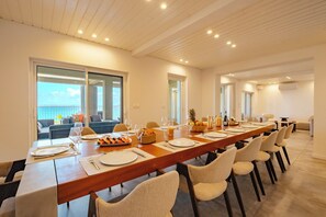 A long dining table set for a meal with chairs, a balcony view, and a modern interior design. - Amazing ocean front 6-bedroom villa in Grand-Case Saint-Martin (Grand-Case)