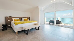 Ein modernes Schlafzimmer mit einem großen Bett, einer Sitzbank und einem Balkon mit Meerblick.