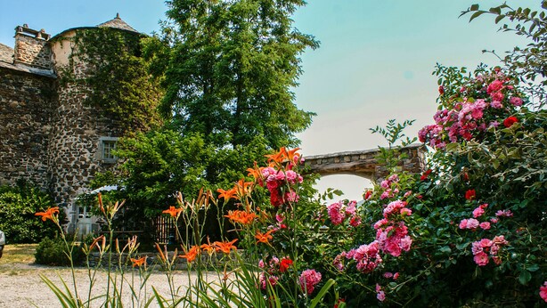 A stone building with ivy, a bridge, and a garden with pink and red flowers. - Bienvenue à la Maison Forte de Chabanolles - Un lieu singulier et authentique (Retournac)