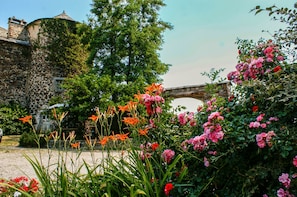 Un edificio de piedra con hiedra, un puente y un jardín con flores rosadas y rojas.