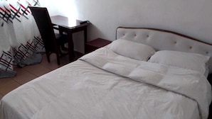 Ein ordentlich bezogenes Bett mit weißer Decke und Kissen, ein Nachttisch aus Holz mit einer Lampe und ein Stuhl.