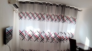 Ein Zimmer mit einem Vorhang mit geometrischem Muster, einem wandmontierten Flachbildfernseher, einem Holztisch und einem Stuhl.