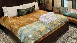 Habitación de hotel con una cama grande, una mesita de noche con lámpara, un ventilador y vistas al exterior a través de una ventana.