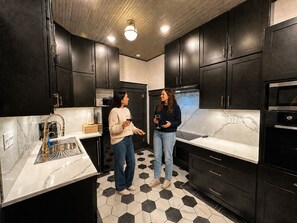 A modern kitchen with dark cabinets, a marble countertop, and a black and white tiled floor.