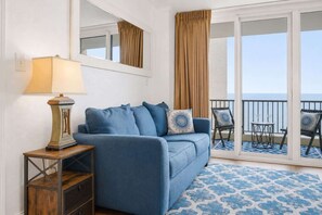 Et værelse med en blå sofa, en lampe, et lille bord og havudsigt fra en balkon.