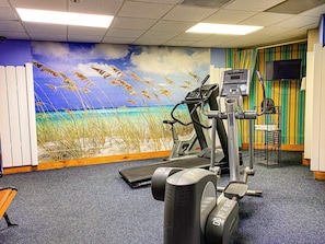 A gym with exercise equipment, a treadmill, and a wall mural of a beach scene. - Ocean View | Pools | Hot Tub | Lazy River (Myrtle Beach)