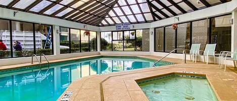 An indoor swimming pool with a glass ceiling, clear pool area, and lounge chairs.