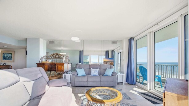 A spacious living room with a grey sofa, a wooden coffee table, and a balcony with a view of the sea. - Serenity Suite Oceanfront w Reclining Sofa (Myrtle Beach)
