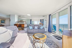 Een ruime woonkamer met een grijze bank, een houten salontafel en een balkon met uitzicht op zee.