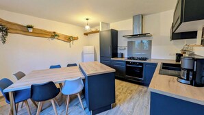 Una cocina moderna con comedor, que incluye una mesa de madera, sillas, refrigerador, horno y cafetera.