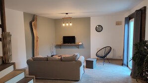 Una sala de estar con un sofá, un televisor en un estante, un sillón y una escalera.