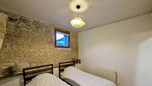 Ein Zimmer mit zwei Betten, einer Steinwand, einem Fenster, einer Heizung und einer Pendelleuchte.