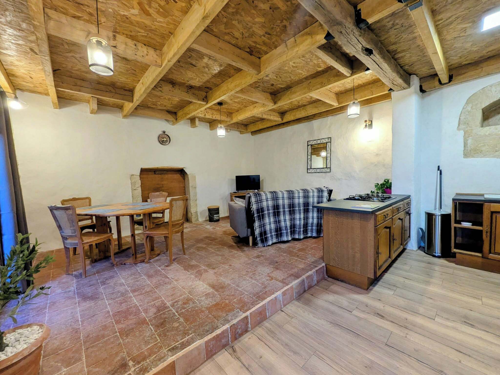 Une cuisine rustique avec des poutres en bois, un coin repas avec une table et des chaises, et un petit espace détente avec une couverture.