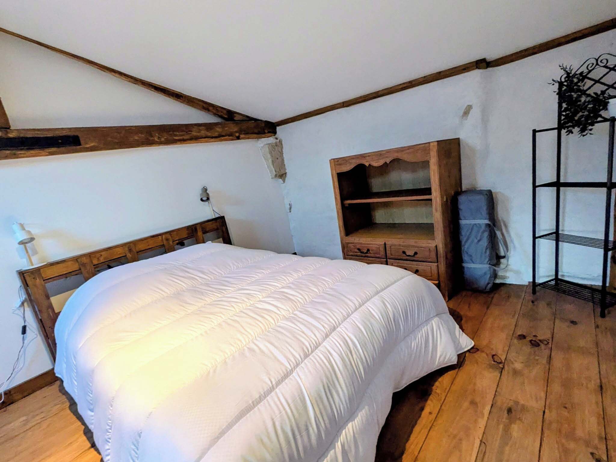 Un dormitorio con estructura de cama de madera, un edredón blanco, un aparador de madera y una estantería metálica.