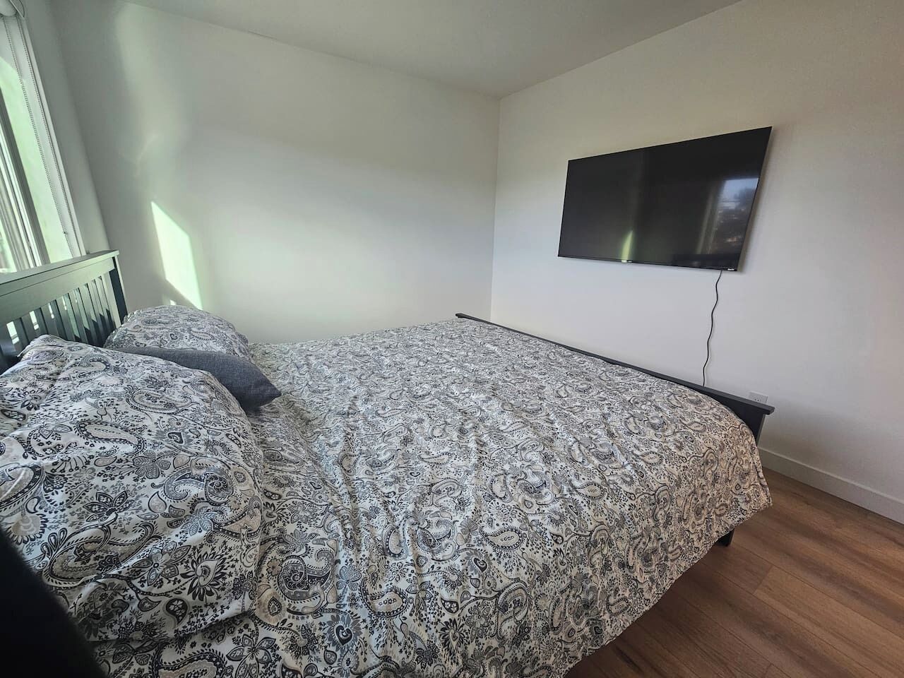 Een slaapkamer met een bed, een aan de muur bevestigde televisie en een raam.