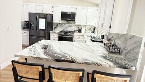 Una cocina moderna con armarios blancos, una isla de mármol y un horno empotrado.