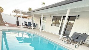 Una piscina con sillones de descanso y un patio cubierto.