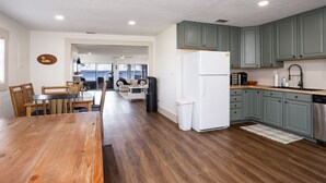 Een moderne keuken met groene kasten, een witte koelkast en een eethoek met een houten tafel en stoelen.