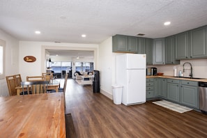 A modern kitchen with green cabinets, a white refrigerator, and a dining area with a wooden table and chairs. - George's Lake House Sunset Special — Florahome, Keystone Heights, Palatka (Florahome)