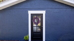 Een donkerblauwe woning met een witte deur en een krans.