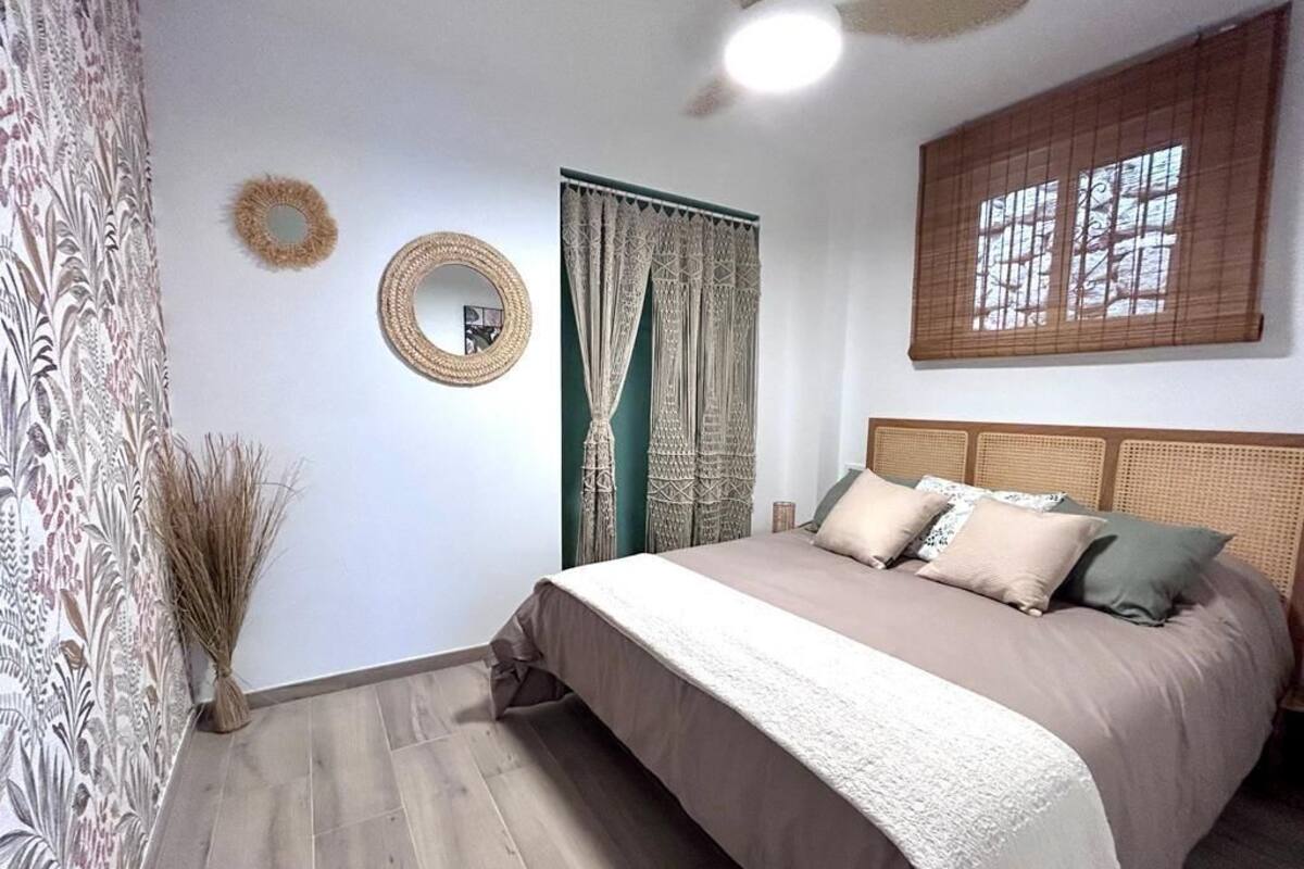 Een slaapkamer met een bed, gordijnen, een spiegel en een raam met jaloezieën.