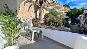 A balcony with a table and chairs, a potted plant, and a stone wall in the background. - Baélia Casa Sabina (Alicante)