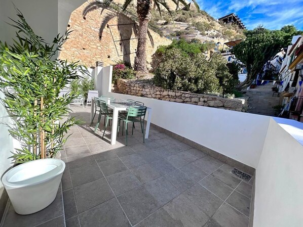 A balcony with a table and chairs, a potted plant, and a stone wall in the background. - Baélia Casa Sabina (Alicante)