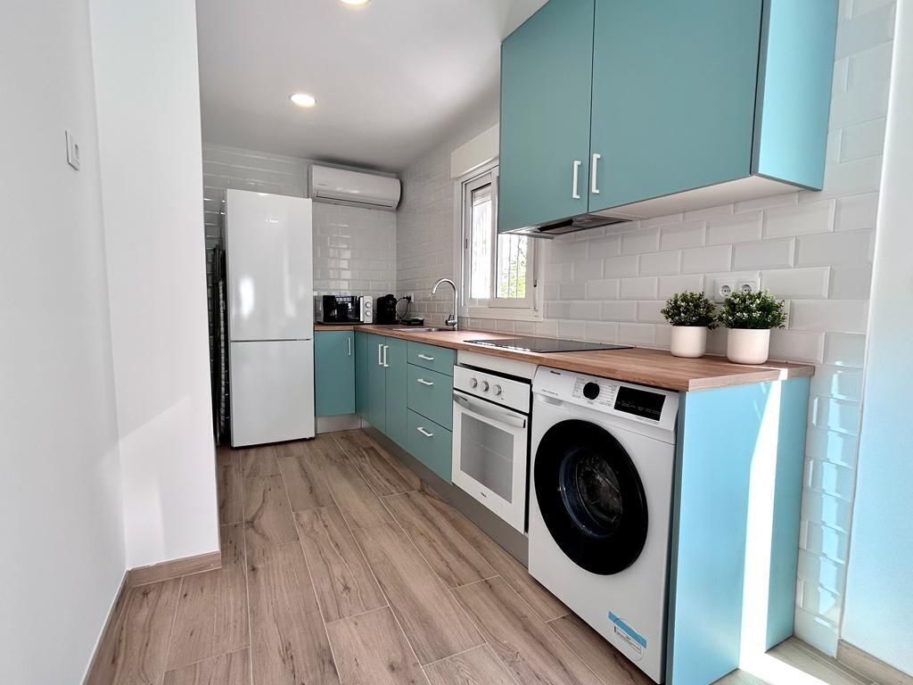 A modern kitchen with teal cabinets, a washing machine, and a coffee maker.