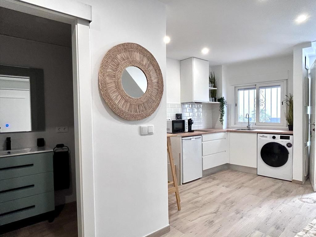 A modern kitchen with white cabinets, a microwave, a washing machine, and a large circular mirror on the wall.
